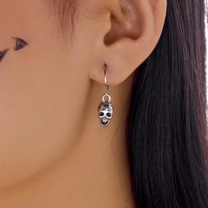 Close-up of vintage silver skull dangle earring with detailed gothic punk engraving