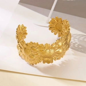 Detailed close-up of a wide gold stainless steel cuff featuring blooming sunflower patterns