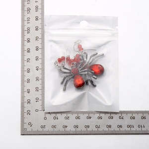 Gros plan de boucles d'oreilles araignée gothique avec cristaux rouges et une règle de mesure