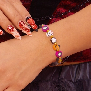 Detalle de pulsera de Halloween con dijes de fantasma y calabaza en la muñeca de la modelo