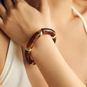 Detail eines Bernstein-Resin-Armbands mit polierten Goldmetallringen am Handgelenk