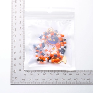 Detailed view of Halloween beaded necklaces with pumpkin and ghost charms in PE packaging