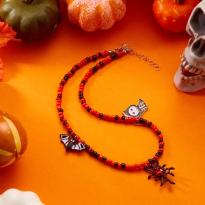 Detail of Halloween beaded necklace featuring spider, bat, and ghost charms on orange background