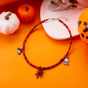 Detail of Halloween beaded necklace with bat, spider, and reaper charms on orange background