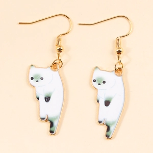 Detailed view of white cartoon cat earrings with green enamel on golden alloy hooks