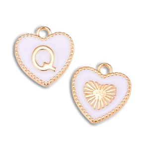 Macro-opname van vergulde hartbedeltjes met roze email en letter Q voor doe-het-zelf sieraden