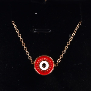 Macro detail of red Evil Eye disc pendant with golden eyelash accents on a fine chain