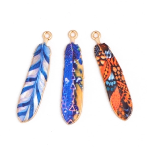 Macro detail of three colorful enamel feather pendants with golden alloy edges for DIY jewelry