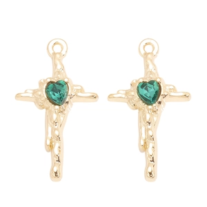 Détail de pendentifs croix texture lave dorée avec cristaux verts en forme de cœur