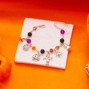 Dettaglio del bracciale di Halloween con ciondoli a zucca e fantasma su sfondo arancio