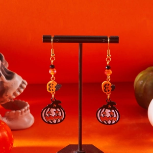 Dettaglio di orecchini a zucca di Halloween con perle arancioni su supporto nero