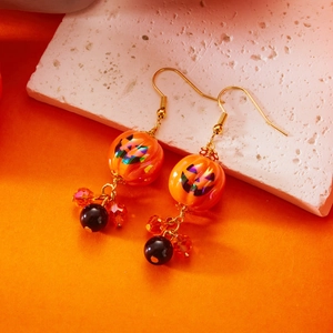 Dettaglio di orecchini a zucca di Halloween con viso Jack-o'-lantern glitterato e perline