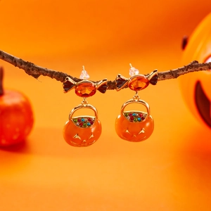 Orecchini di Halloween con cesti di zucca dorati su rami e sfondo arancione vivace