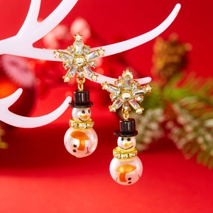 Detailed close-up of snowman earrings with pearl body and crystal snowflake stud on a stand