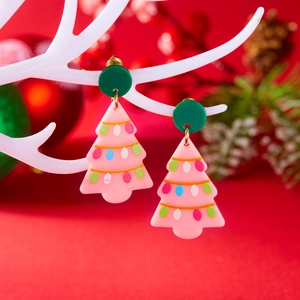Detailopname van de lichte roze acryl kerstboom oorbellen tegen een feestelijke rode decor