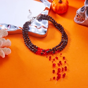 Gothic Halloween multilayered beaded necklace with red tassels and skull decor on orange background