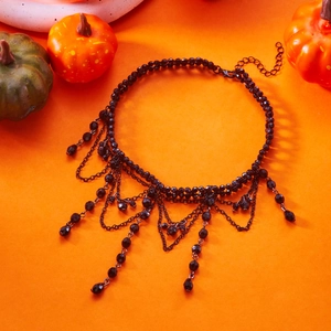 Gothic multi-layer black beaded choker with tassel charms on vibrant orange pumpkin background