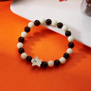 Macro shot of Halloween ghost charm and black-and-white beaded bracelet on orange backdrop