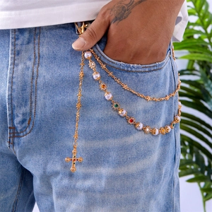 Detail of gold multilayer pants chain with pearls, colored gems and cross pendant