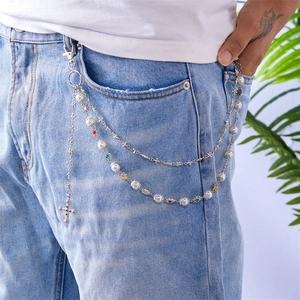Detail of multilayer silver pants chain with pearls and cross pendant on denim