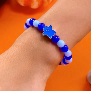 Close-up of blue beaded Halloween ghost bracelet worn against a vibrant orange background