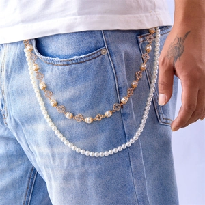 Detail of double-layer punk waist chain with white pearls and golden clover on blue jeans