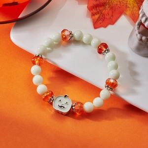 Macro detail of Halloween bracelet with pumpkin charm and festive beads on orange background