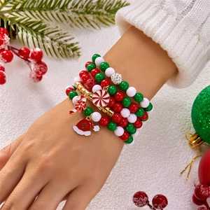 Detail von weihnachtlichen Mehrlagen-Perlenarmbändern mit Anhängern auf weißem Strickärmel