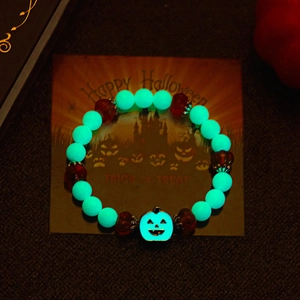 Luminous Halloween beaded bracelet with pumpkin charm glowing in a dark festive setting