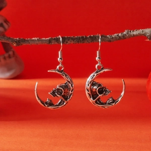 Gothic silver crescent moon and skull earrings displayed on a rustic branch background