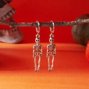 Macro detail of silver skeleton drop earrings hanging on a dry tree branch for Halloween