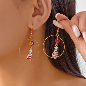 Detail shot of a large golden hoop earring featuring a white enamel Christmas tree pendant