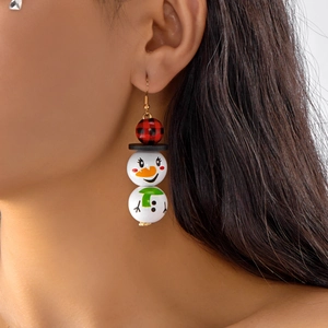 Gros plan de boucles d'oreilles bonhomme de neige festives avec perles rouges à carreaux