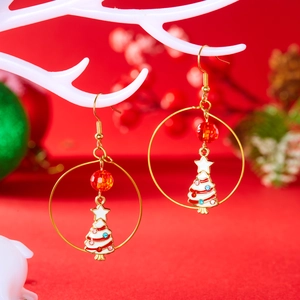Detail of Christmas earrings with gold rings, red crystal beads, and enamel trees on red background