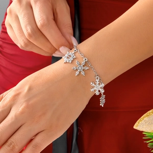 Silver chain bracelet featuring delicate snowflake charms on a festive red background