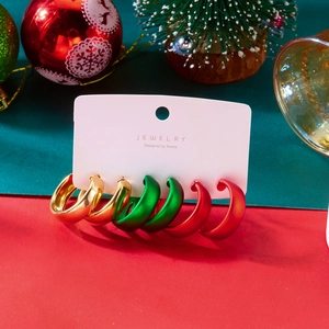 Tre paia di orecchini natalizi intrecciati in rosso, verde e oro metallizzato su carta