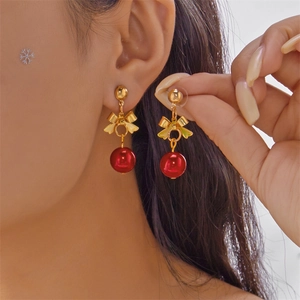 Close-up of red pearl earrings with golden bow detail and festive Christmas style