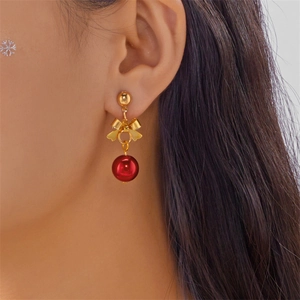 Close-up of golden bow earrings with red beads shown on model for festive holiday style