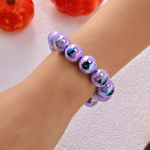 Dettaglio del bracciale con perline viola iridescenti e motivi festivi di gatti di Halloween