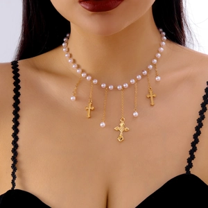 Détail du collier de perles croix avec pompons dorés sur fond de dentelle noire
