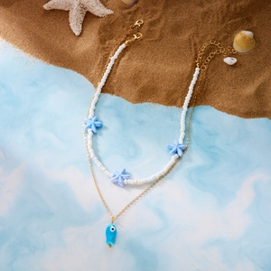 Detail of layered ocean necklace with ceramic fish pendant and star beads on a beach background
