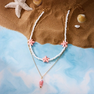Detail of a layered ocean necklace with pink starfish beads and a golden fish pendant