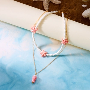 Detail of beaded necklace with pink ceramic fish pendant and starfishes on beach sand