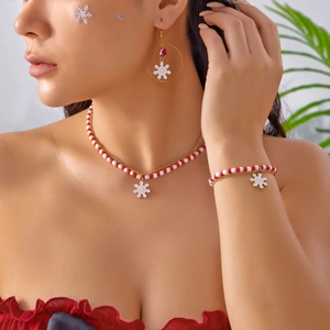 Primo piano di un modello che indossa un set di gioielli natalizi con perline rosse e fiocco