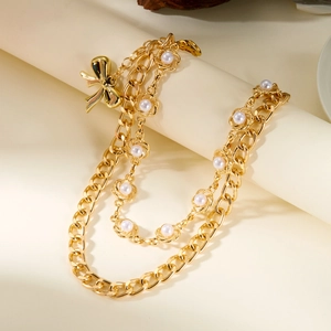 Détail de la chaîne dorée avec pendentif papillon et perles sur fond beige doux