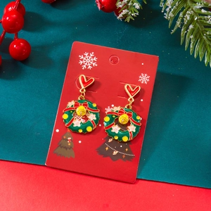 Détail de boucles d'oreilles couronne de Noël avec nœuds rouges et grelots sur carte