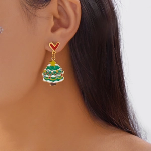 Gros plan d'un modèle portant des boucles d'oreilles sapin de Noël avec clou cœur rouge