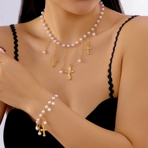 Gros plan d'un ensemble collier de perles roses et pendentifs croix dorées