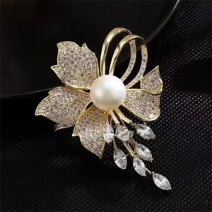 Gros plan d'une broche fleur dorée ornée de zircons brillants et d'une perle blanche