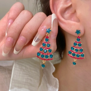 Close-up of model wearing sparkling Christmas tree tassel earrings with heart crystals